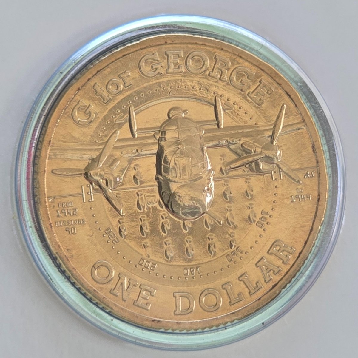 Gold-colored 2014 $1 reverse of coin with airplane design and text ' G for George One Dollar From 1942 To 1944 Missions 90'