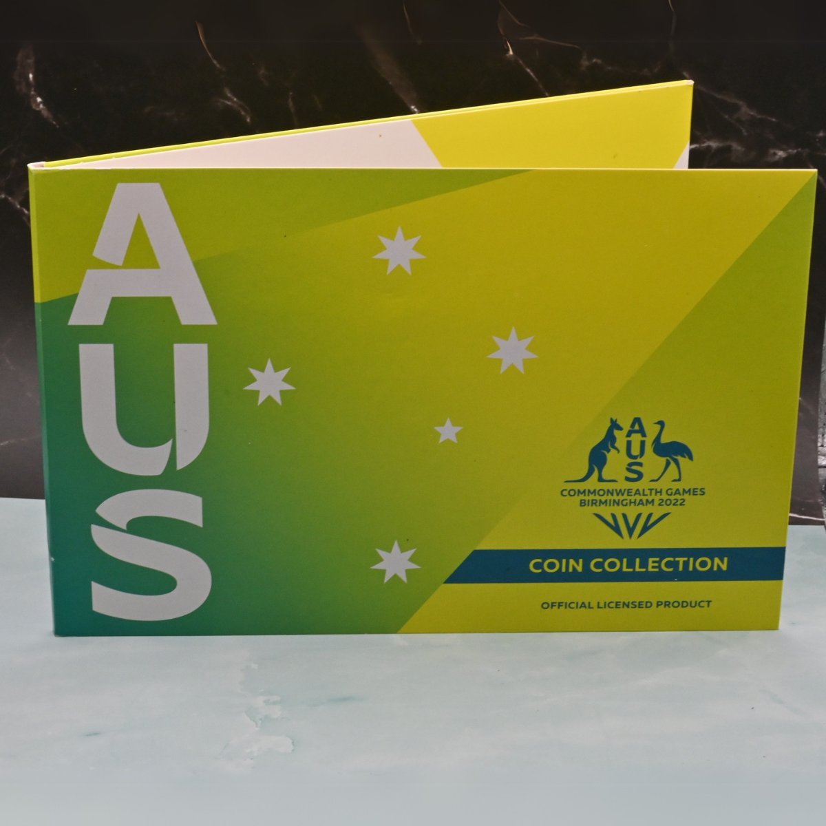 Seven coin Commonwealth Games Birmingham collection folder with 'AUS' - kangaroo and emu emblem on a green and yellow background