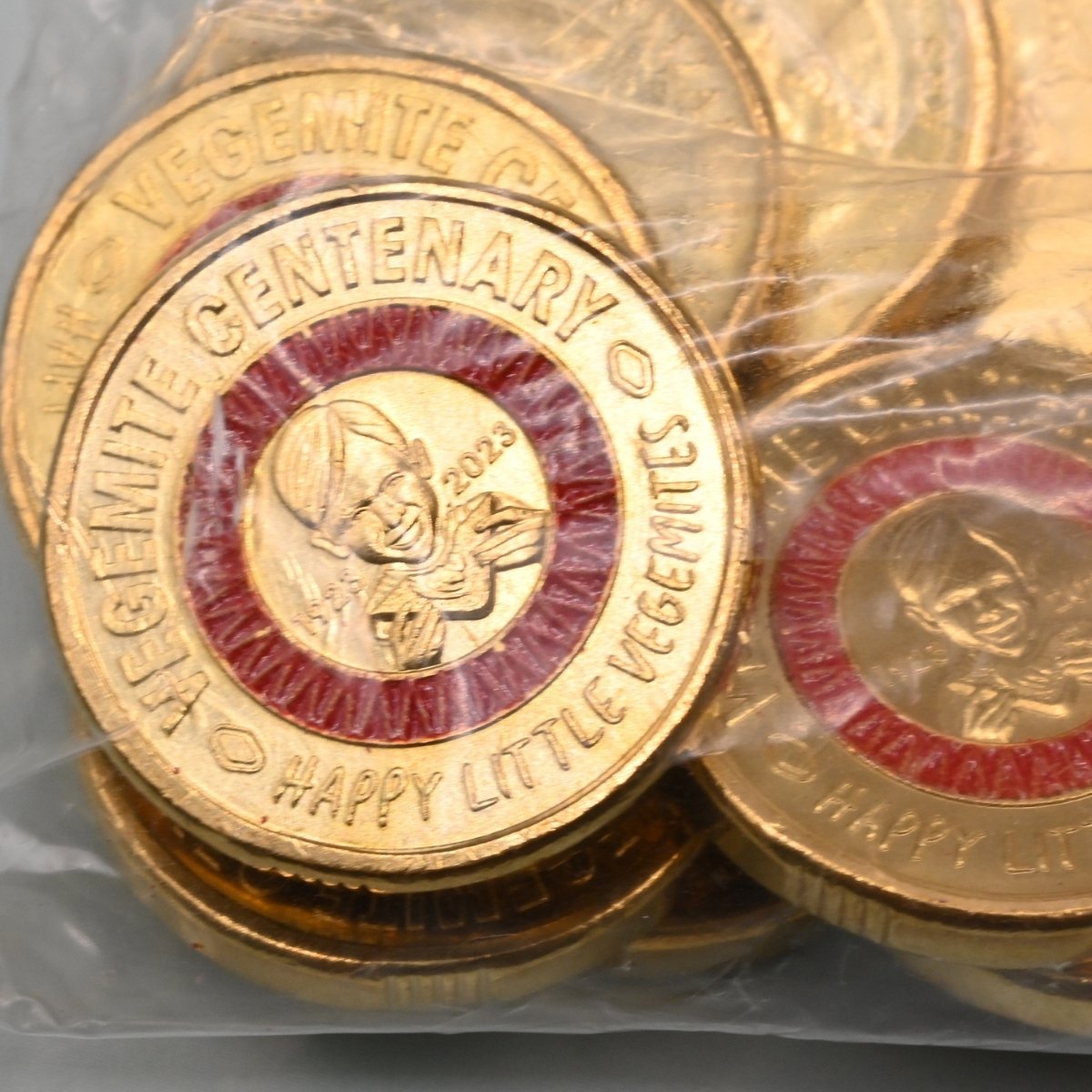 2023 $2 close up of reverse side of coins with 'Vegemite Centenary' text and red colour design, in security bag.