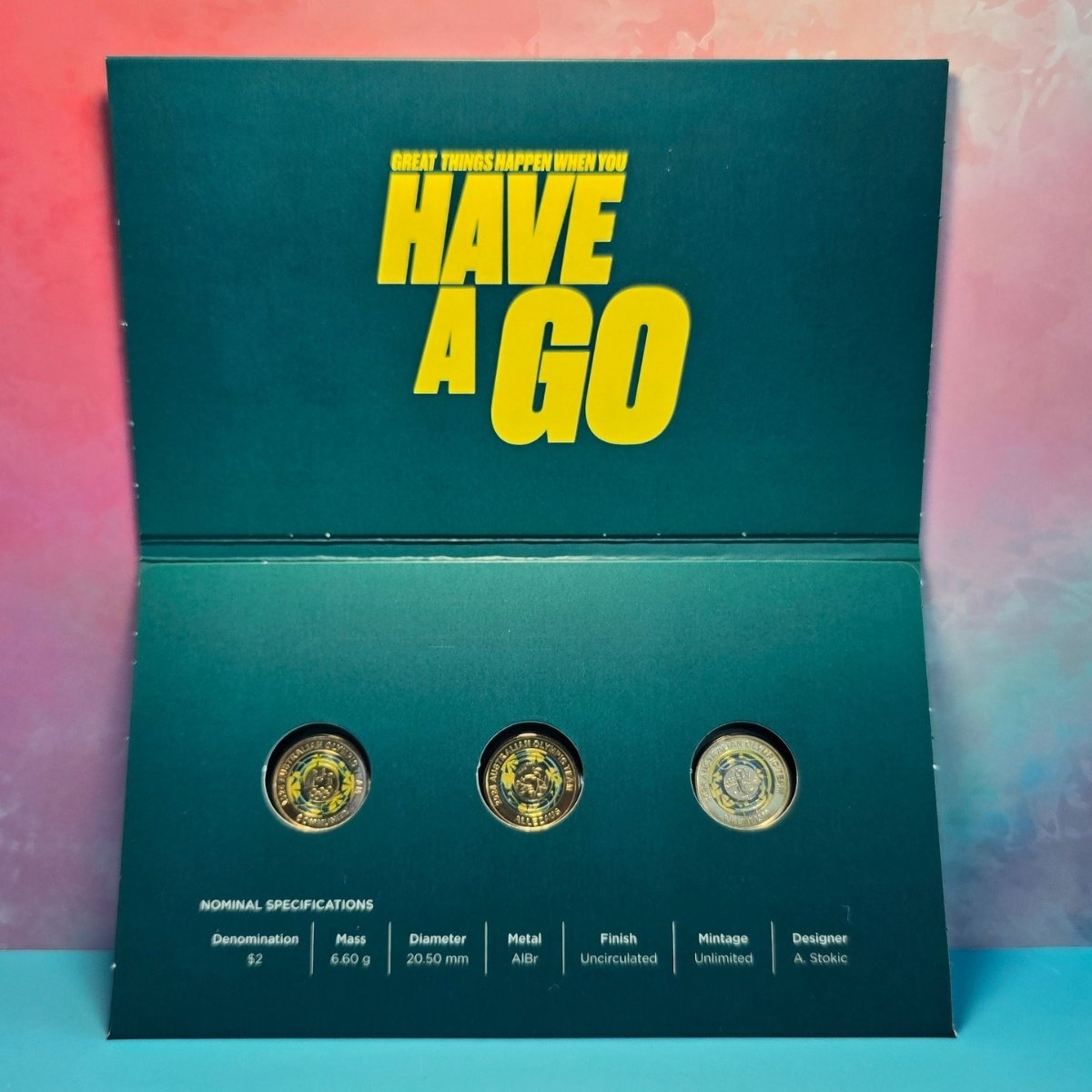 Set of three $2 coloured coins in a green holder with yellow text 'Great Things Happen When You Have A Go' and nominal specifications