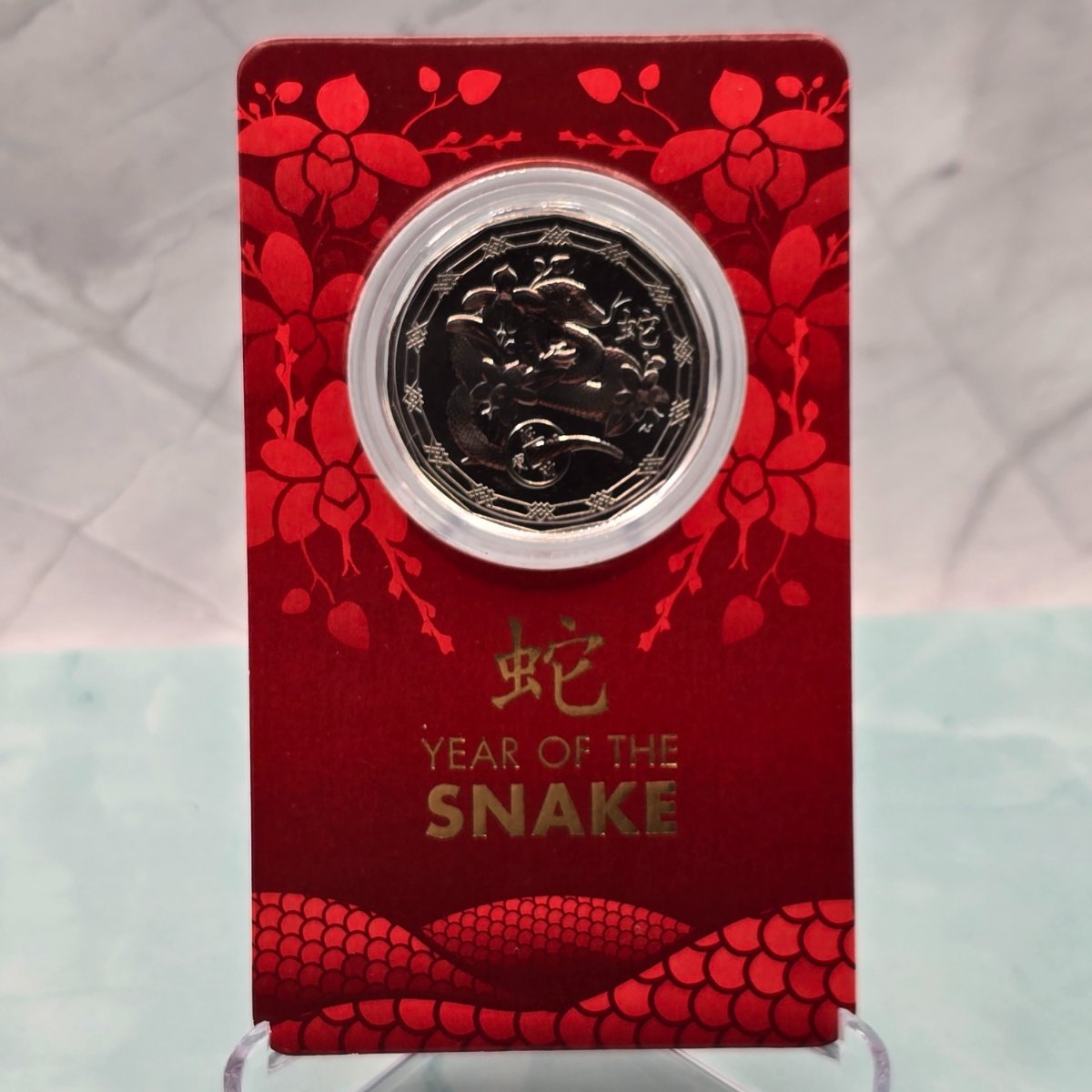 2025 50c Lunar Year of the Snake 50c Uncirculated Coin Tetra Decagon Series front of red small RAM card with gold accent